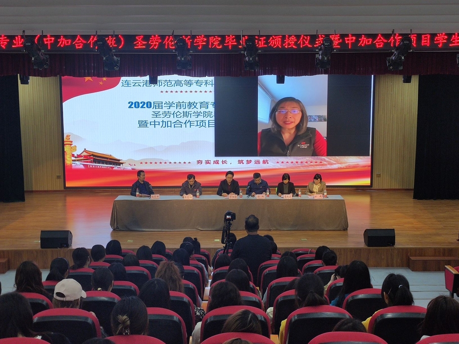Ining Chao appears on a large screen in an auditorium. She is addressing the graduates, who are seated in the audience.